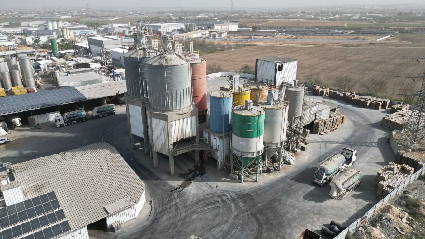 יצרן מלט במפעל תעשייתי גדול המציג מתקני אחסון וייצור מלט לצד משאיות הובלה.